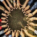 A diverse group of hands forming a star shape in a circle on grassy ground, symbolizing unity.