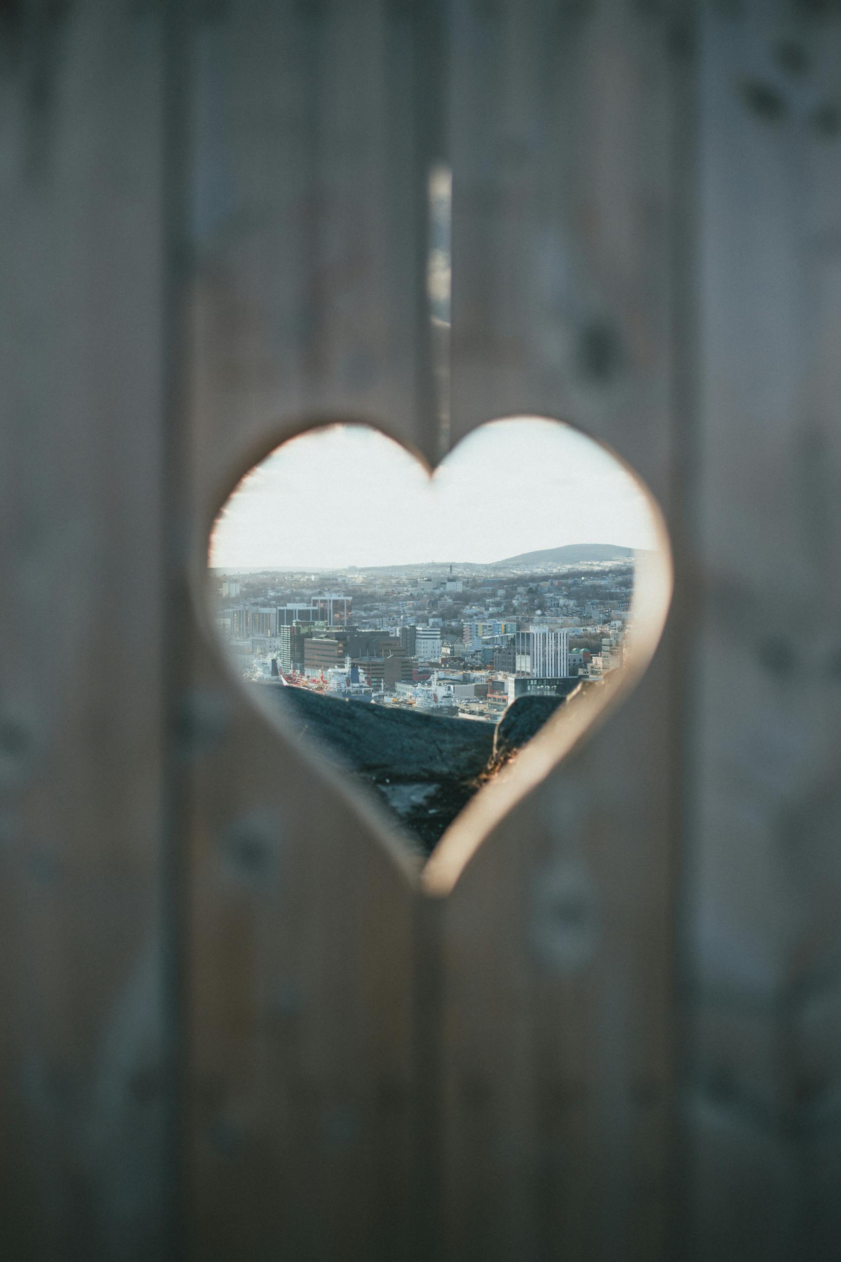 Unique cityscape view through a heart-shaped wooden cutout, showcasing urban life.